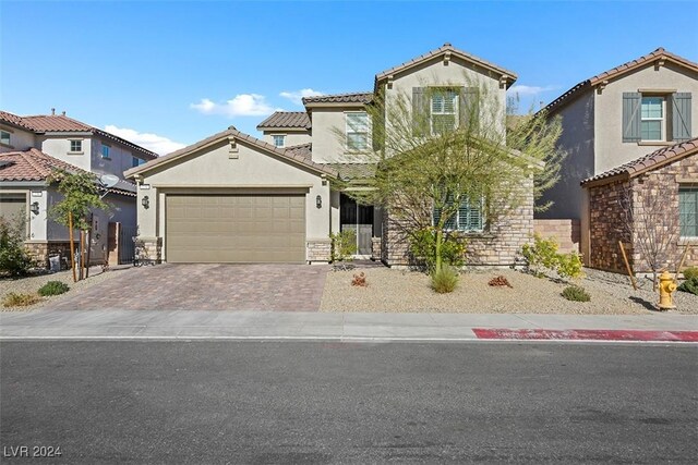 mediterranean / spanish house with stucco siding, a tile roof, decorative driveway, stone siding, and a garage