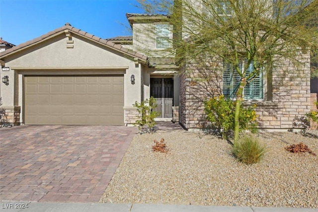 view of front of property with decorative driveway, stone siding, a tile roof, and stucco siding