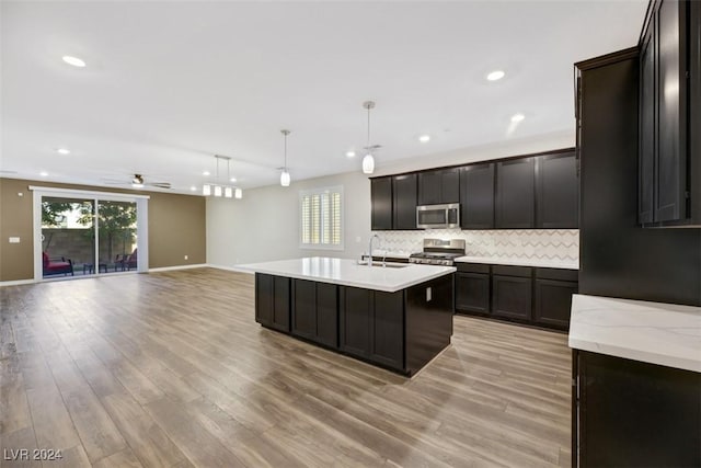 kitchen featuring a center island with sink, a sink, light wood-style floors, appliances with stainless steel finishes, and decorative backsplash