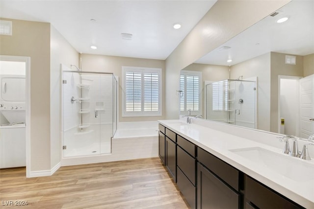 bathroom featuring wood finished floors, a stall shower, a sink, stacked washer / dryer, and a bath