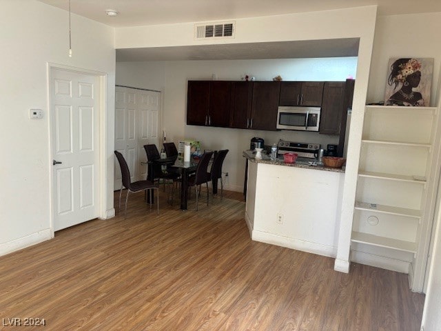 kitchen with dark brown cabinets, wood-type flooring, stainless steel appliances, and dark stone counters