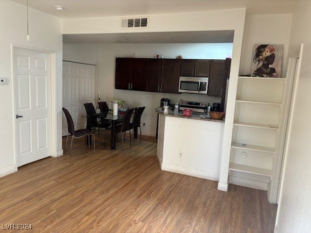 kitchen featuring hardwood / wood-style flooring, dark brown cabinets, stainless steel appliances, and dark stone counters