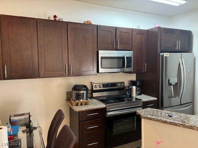 kitchen featuring dark brown cabinetry, light stone countertops, and stainless steel appliances