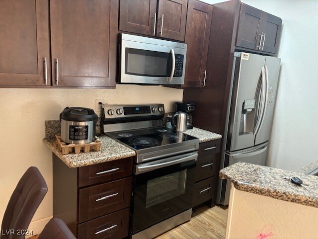 kitchen featuring light stone countertops, dark brown cabinets, stainless steel appliances, and light hardwood / wood-style floors