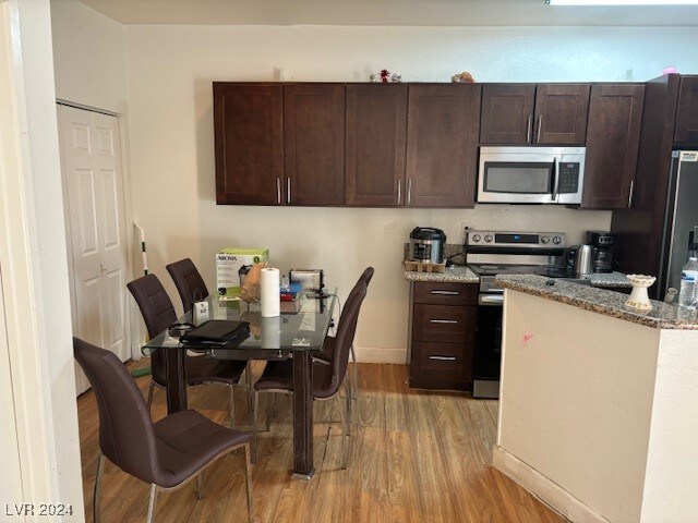 kitchen featuring light stone counters, light hardwood / wood-style flooring, dark brown cabinets, and appliances with stainless steel finishes