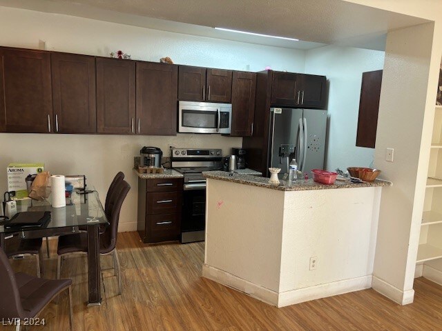 kitchen with dark brown cabinetry, light stone countertops, light hardwood / wood-style flooring, and appliances with stainless steel finishes