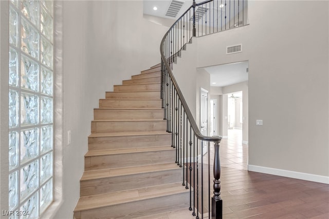 stairs featuring plenty of natural light, wood-type flooring, and a towering ceiling