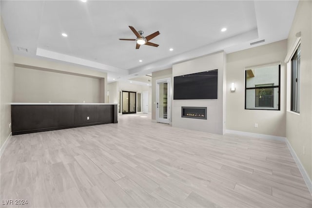 unfurnished living room with light wood-type flooring, a tray ceiling, and ceiling fan