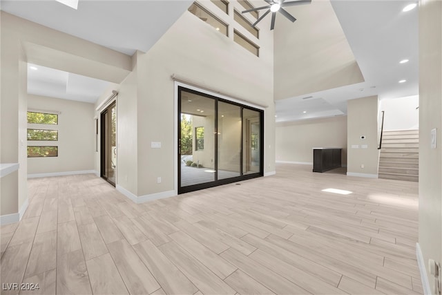 unfurnished living room with a tray ceiling, ceiling fan, and light hardwood / wood-style flooring