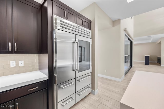 kitchen with dark brown cabinets, light hardwood / wood-style floors, stainless steel built in refrigerator, and tasteful backsplash