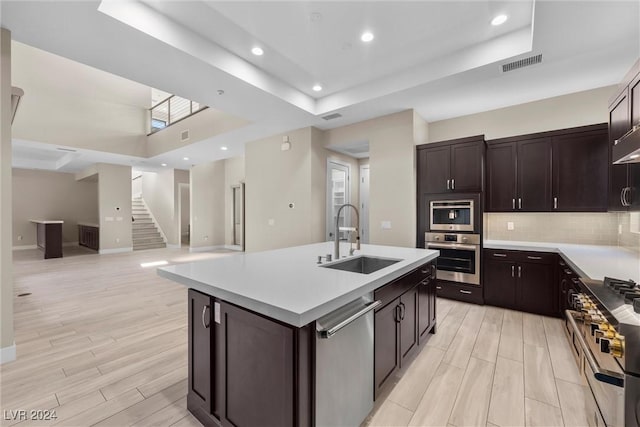 kitchen with sink, stainless steel appliances, light hardwood / wood-style flooring, backsplash, and a center island with sink