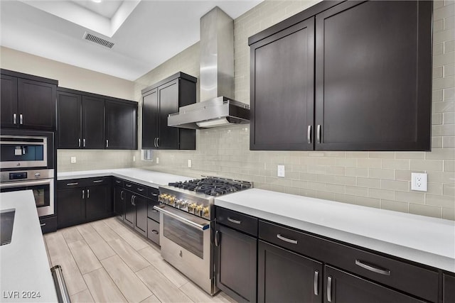 kitchen featuring appliances with stainless steel finishes, tasteful backsplash, light hardwood / wood-style floors, and wall chimney range hood