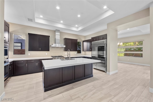 kitchen featuring a tray ceiling, sink, and wall chimney range hood