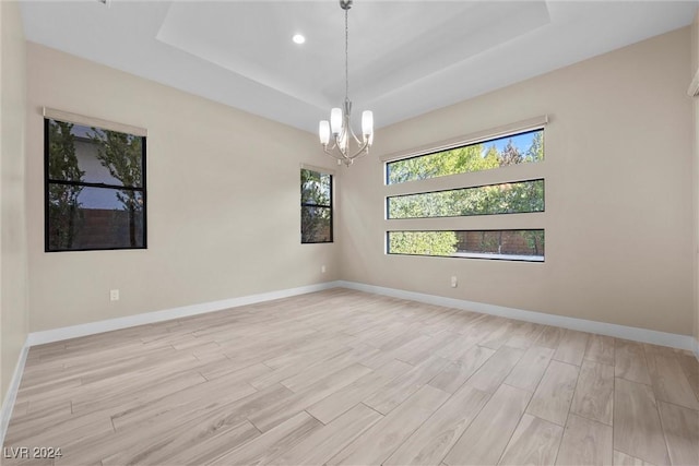 spare room featuring light hardwood / wood-style floors, a tray ceiling, and a notable chandelier