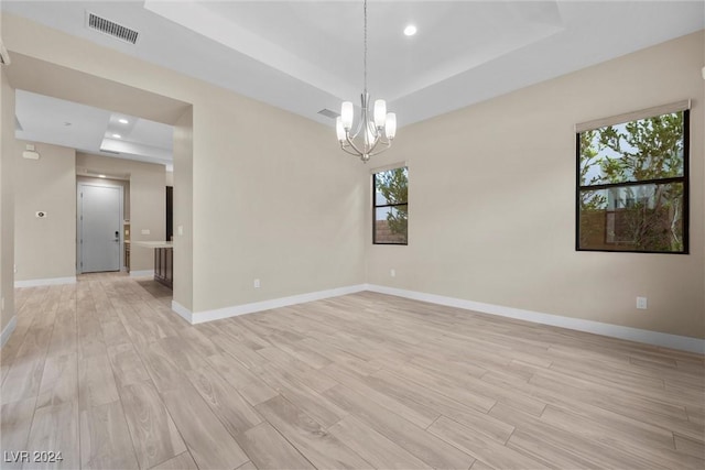 unfurnished room featuring light hardwood / wood-style floors, a raised ceiling, and a chandelier