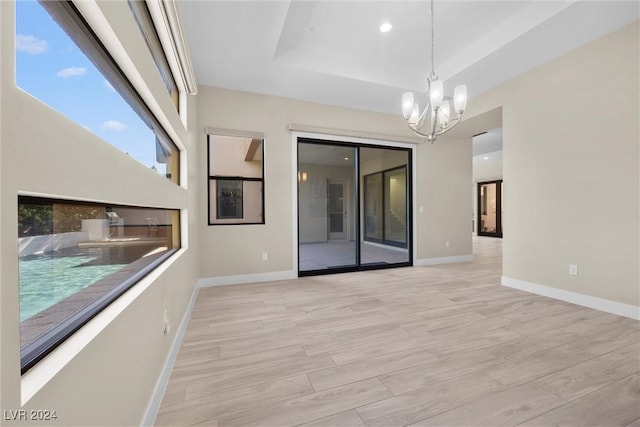 unfurnished room with a tray ceiling, a chandelier, and light hardwood / wood-style floors