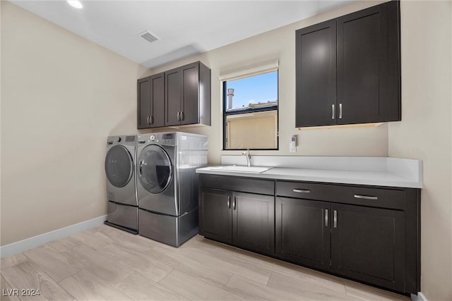 laundry area featuring cabinets, separate washer and dryer, sink, and light wood-type flooring