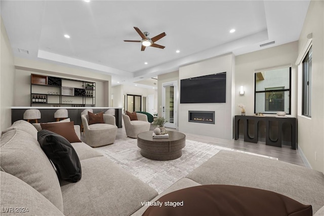 living room with a tray ceiling, ceiling fan, and light hardwood / wood-style floors