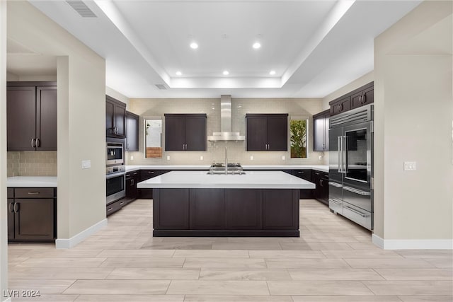 kitchen featuring a kitchen island with sink, stainless steel built in fridge, wall chimney exhaust hood, and dark brown cabinets