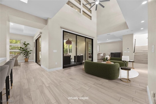 living room with ceiling fan, a raised ceiling, a towering ceiling, and light hardwood / wood-style flooring