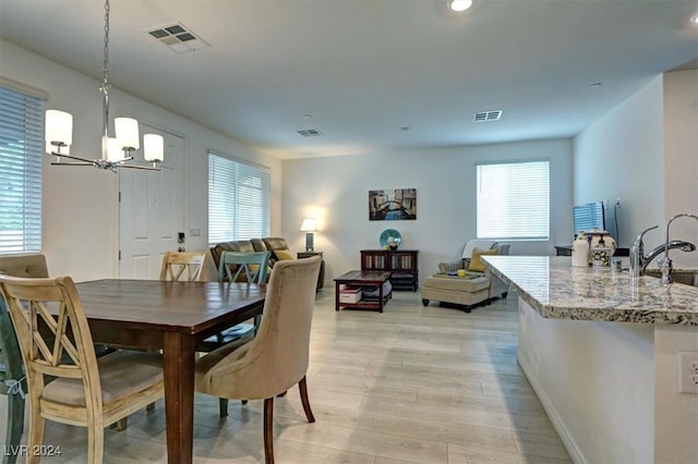 dining space with an inviting chandelier, sink, and light hardwood / wood-style flooring