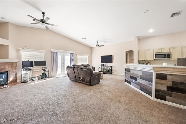 living room with high vaulted ceiling, ceiling fan, light colored carpet, and a tile fireplace