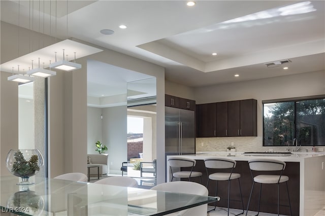 kitchen with sink, built in refrigerator, decorative backsplash, dark brown cabinets, and a breakfast bar area