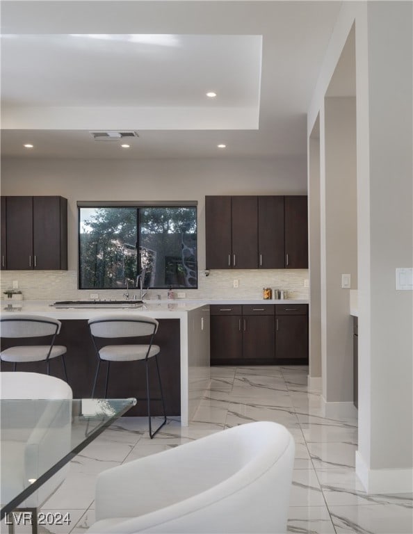 kitchen with backsplash, a breakfast bar, and dark brown cabinets