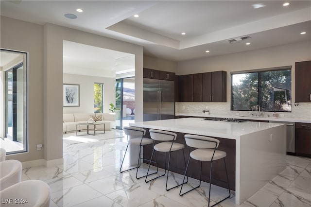 kitchen featuring dark brown cabinets, a center island, backsplash, and a wealth of natural light