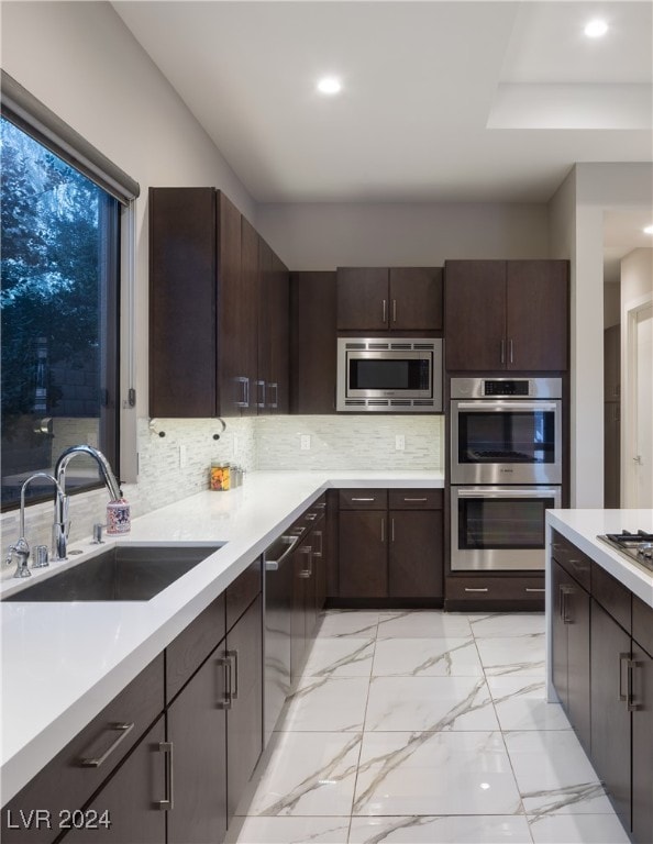 kitchen with appliances with stainless steel finishes, tasteful backsplash, dark brown cabinets, and sink