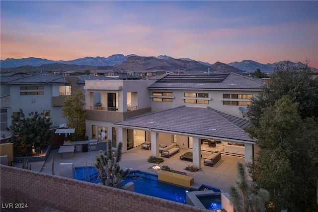 back house at dusk with a mountain view, a fenced in pool, an outdoor hangout area, a balcony, and a patio area