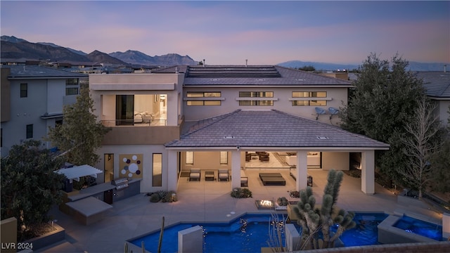 back house at dusk featuring a mountain view, a patio, a balcony, and a pool with hot tub