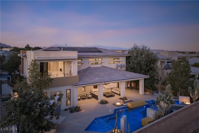 back house at dusk featuring outdoor lounge area, a patio area, and a balcony