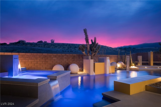 pool at dusk with an in ground hot tub and pool water feature