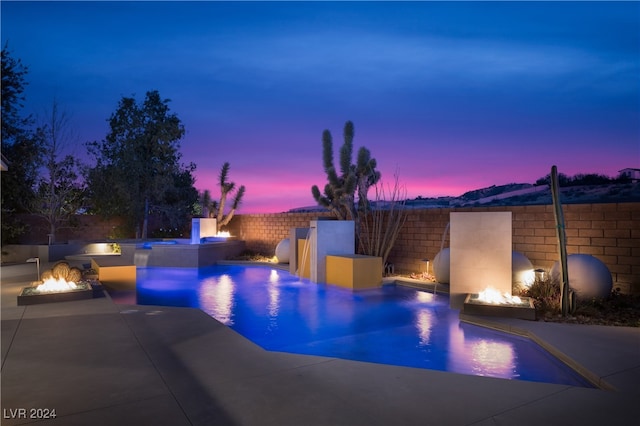 pool at dusk featuring pool water feature, a hot tub, an outdoor fire pit, and a patio area