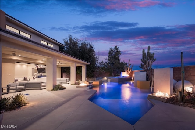 pool at dusk with ceiling fan, a patio, and an outdoor hangout area