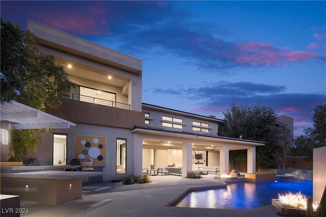 back house at dusk featuring an outdoor hangout area, ceiling fan, a balcony, exterior kitchen, and a patio