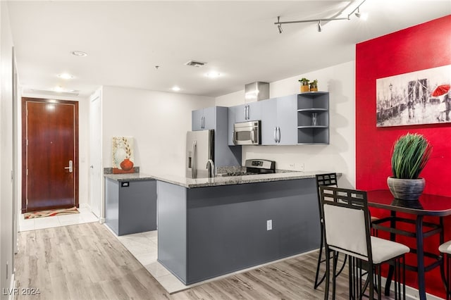 kitchen with track lighting, light hardwood / wood-style flooring, dark stone countertops, kitchen peninsula, and stainless steel appliances