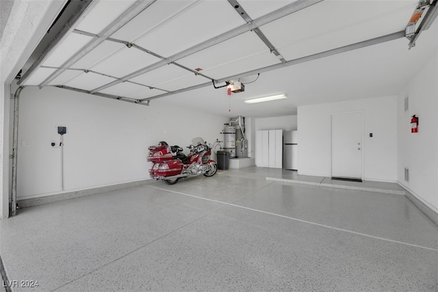 garage featuring stainless steel refrigerator, strapped water heater, and a garage door opener