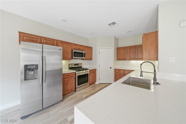 kitchen with kitchen peninsula, light wood-type flooring, sink, and appliances with stainless steel finishes