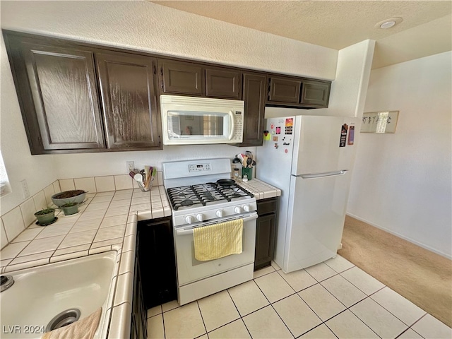 kitchen with light carpet, dark brown cabinets, white appliances, a textured ceiling, and tile countertops