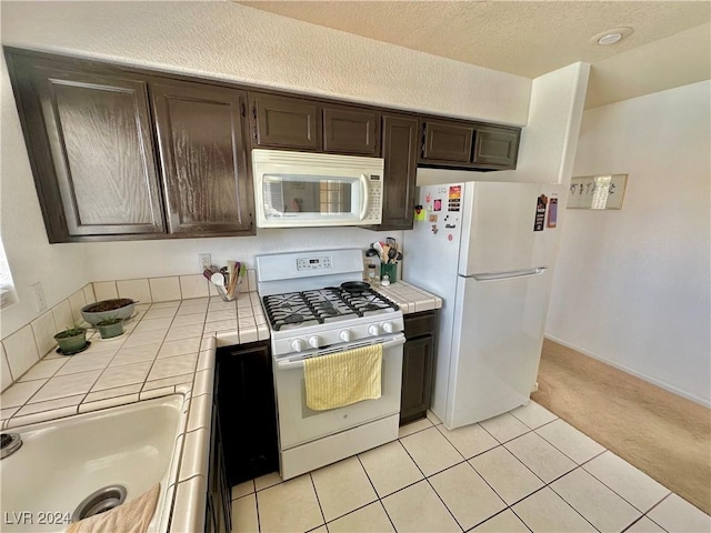 2153 Camel Mesa Dr, Laughlin, NV 89029 - kitchen featuring tile counters, white appliances, dark brown cabinetry, and light carpet