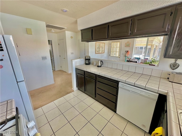 kitchen featuring dark brown cabinetry, tile countertops, light colored carpet, and white appliances