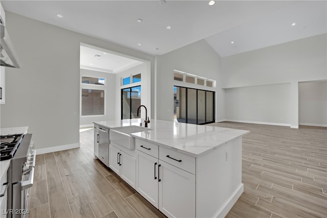 kitchen with a center island with sink, white cabinets, sink, and light hardwood / wood-style flooring