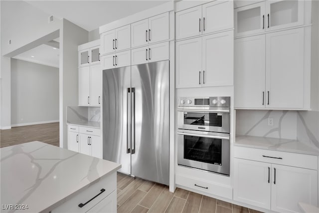 kitchen featuring light stone countertops, appliances with stainless steel finishes, backsplash, light hardwood / wood-style floors, and white cabinetry