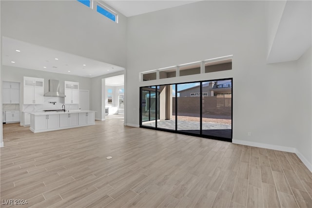 unfurnished living room with sink, a high ceiling, and light hardwood / wood-style flooring