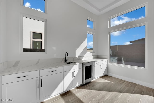 kitchen with light stone countertops, sink, beverage cooler, white cabinets, and light wood-type flooring