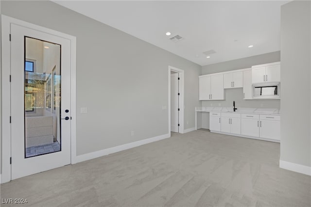 kitchen featuring white cabinetry, sink, white microwave, and light colored carpet