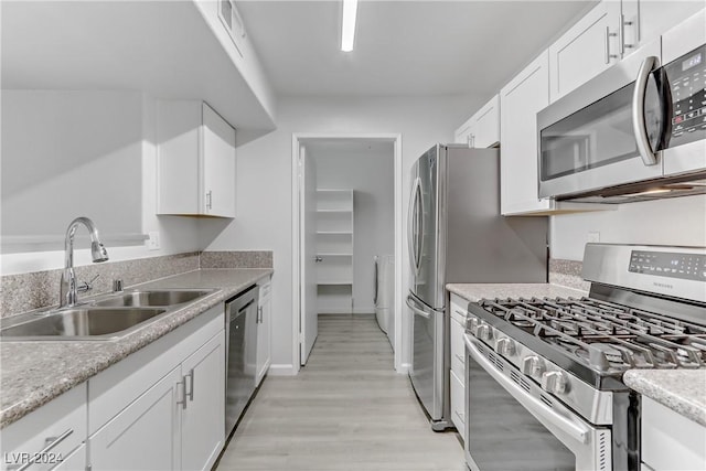 kitchen featuring sink, light hardwood / wood-style flooring, stainless steel appliances, white cabinets, and washer / dryer