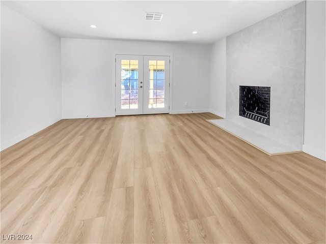 unfurnished living room featuring french doors, light wood-type flooring, and a large fireplace